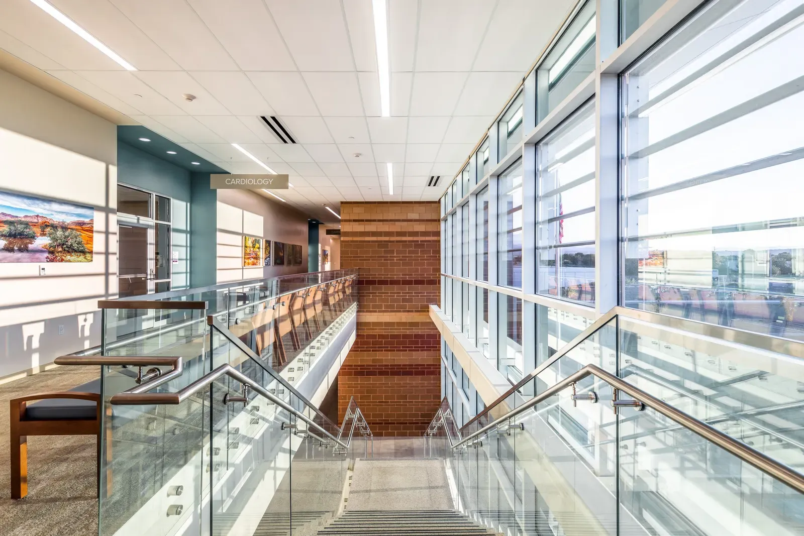 Open stair and balcony with glass railings beside a tall window wall, with a Cardiology sign ahead
