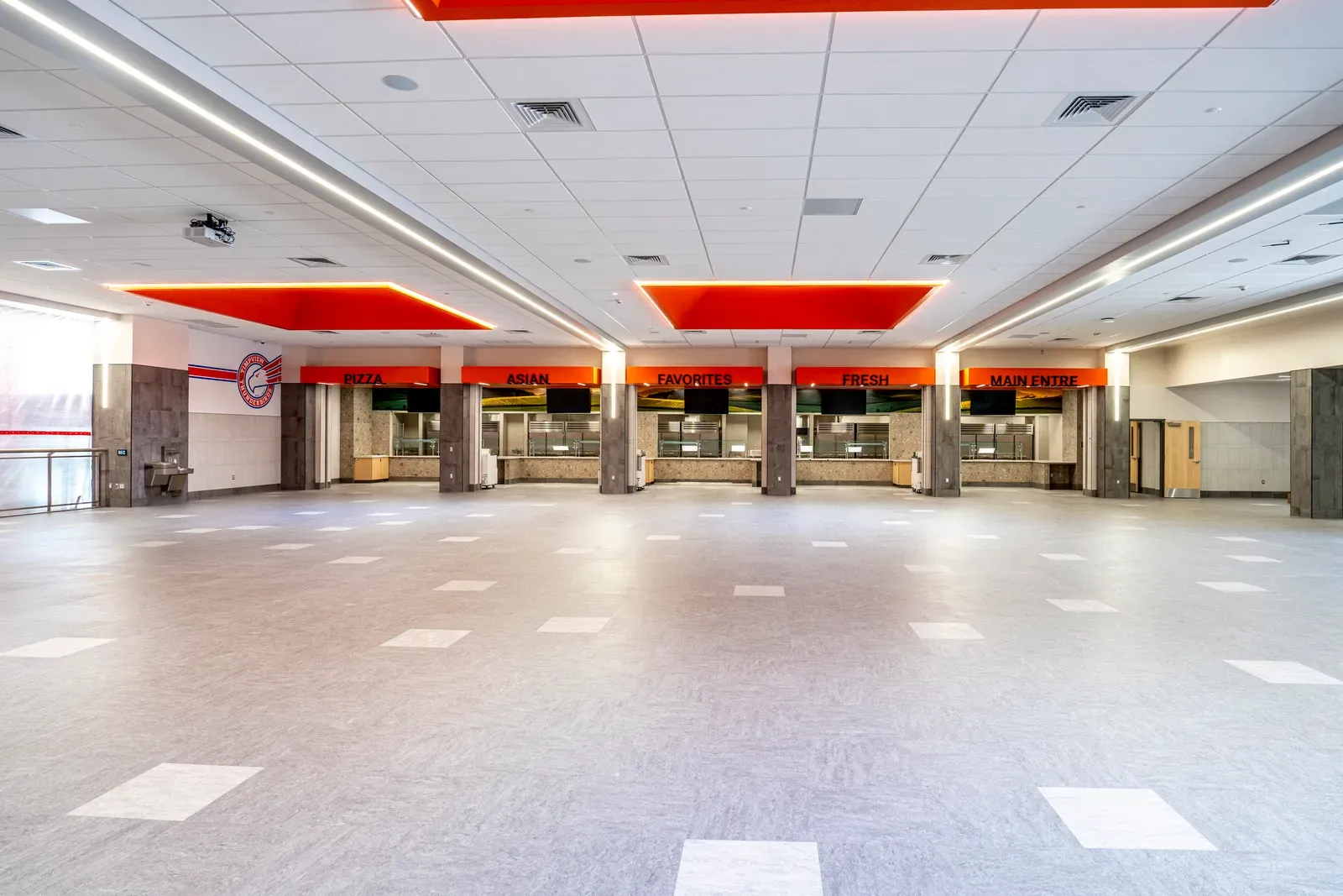 Wide cafeteria floor with food-service counters under orange ceiling panels along the far wall.