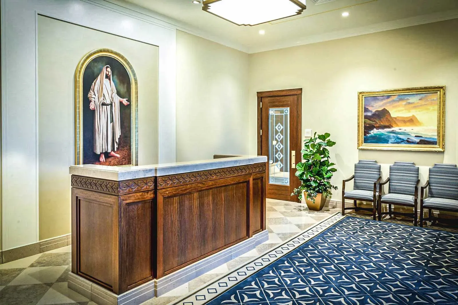 Lobby with a carved wood reception desk, a painting of a robed figure, a seascape painting and a blue patterned rug.