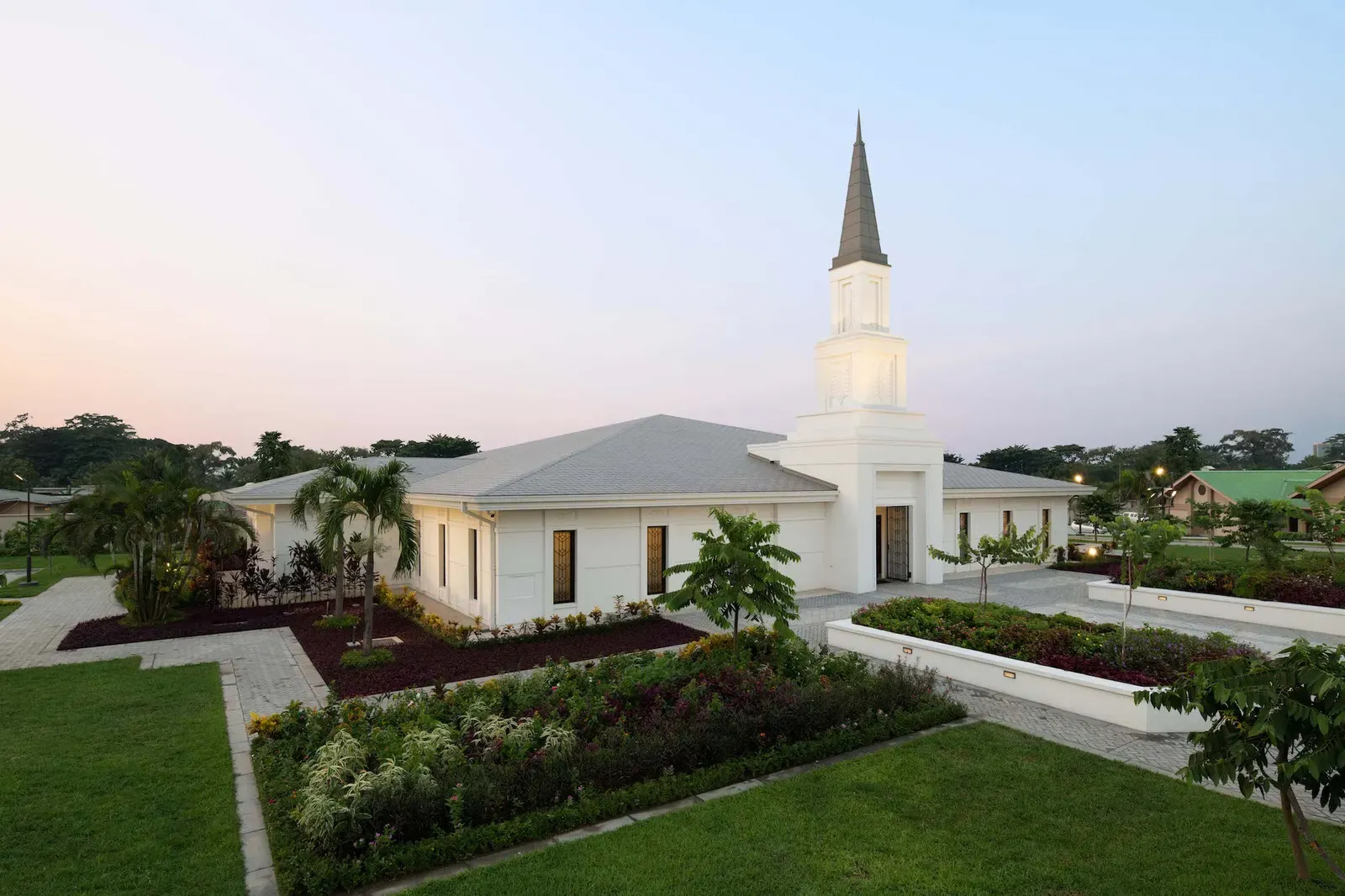 Temple seen from above at dusk, with white walls, a gray roof, a spire, and landscaped flower beds