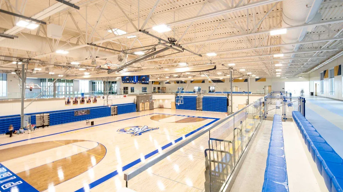 Gymnasium with a hardwood court, blue bleachers, and an upper running track