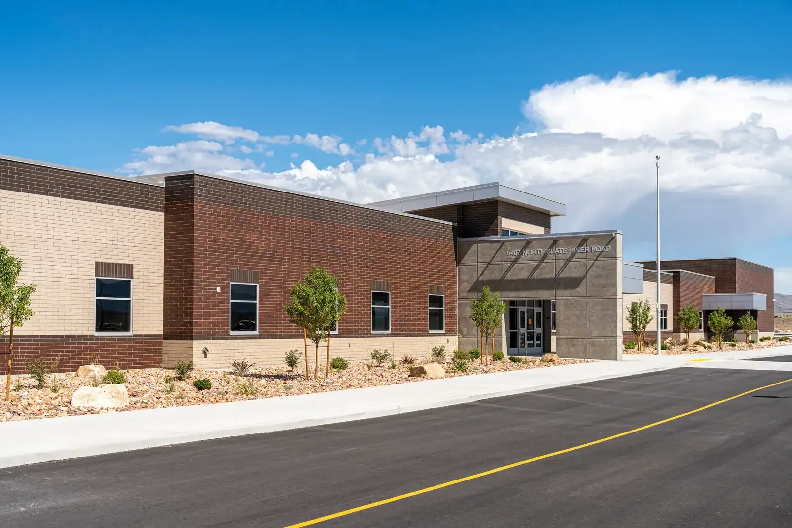 Side of the school with brick and tan block walls, a recessed concrete entrance and a long drive in front.