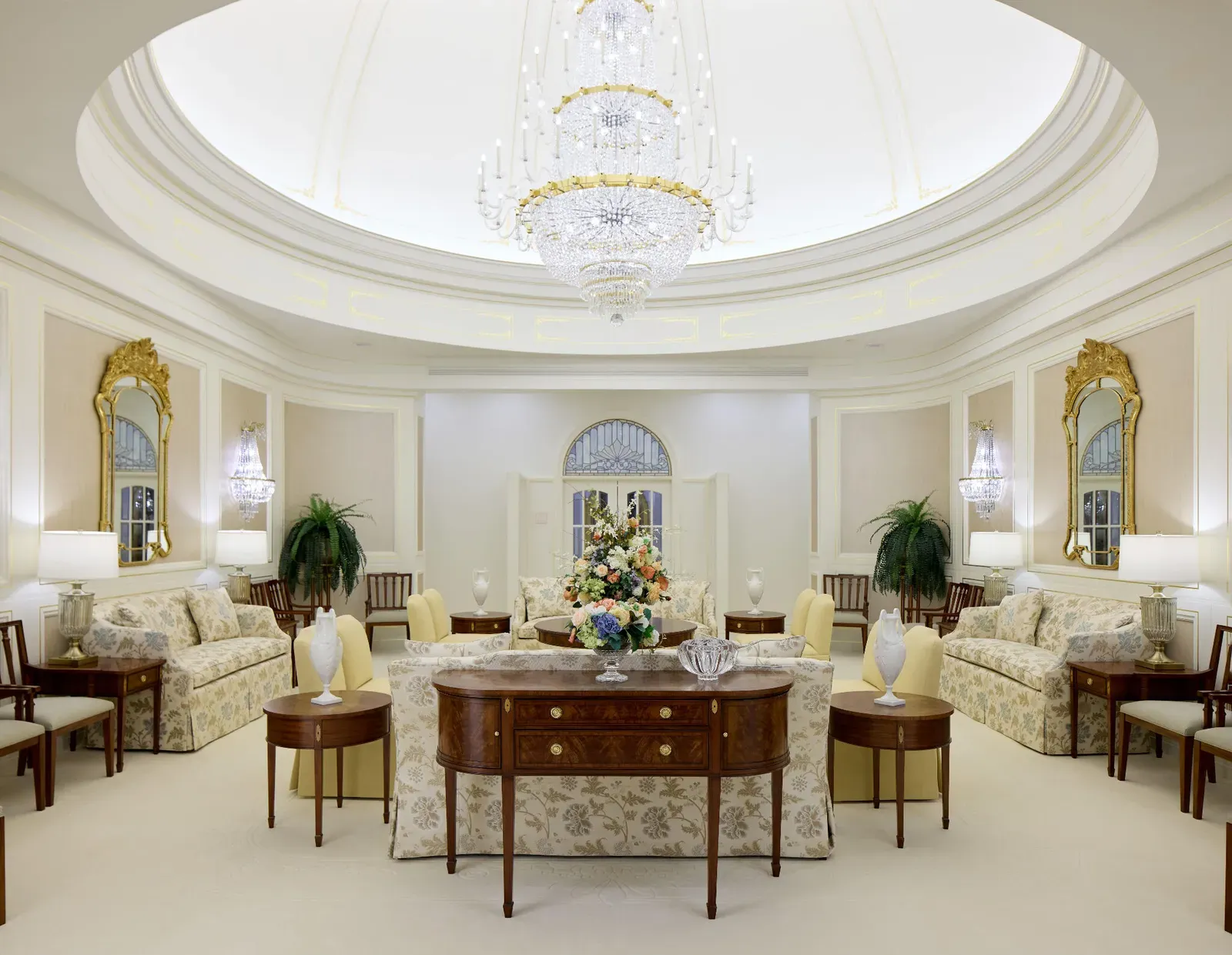 Round room with a domed ceiling, a crystal chandelier, floral sofas, gold-framed mirrors and a sideboard topped with flowers
