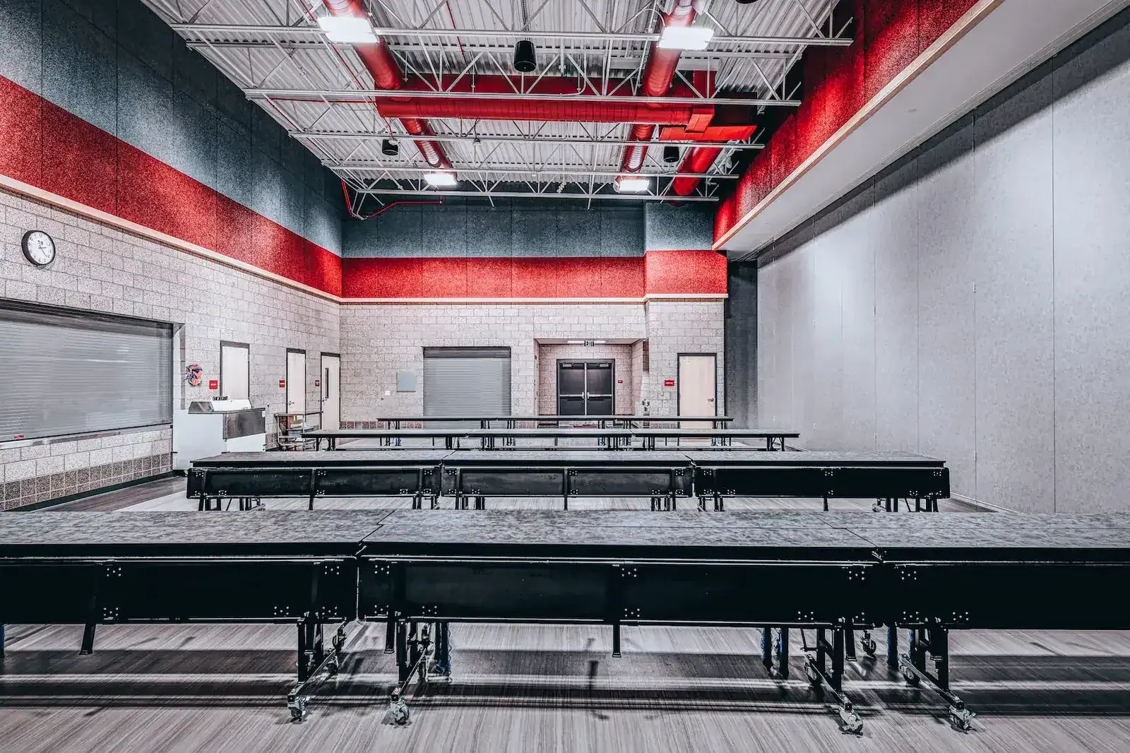 Lunchroom with long folding tables, red and gray walls and exposed steel roof trusses