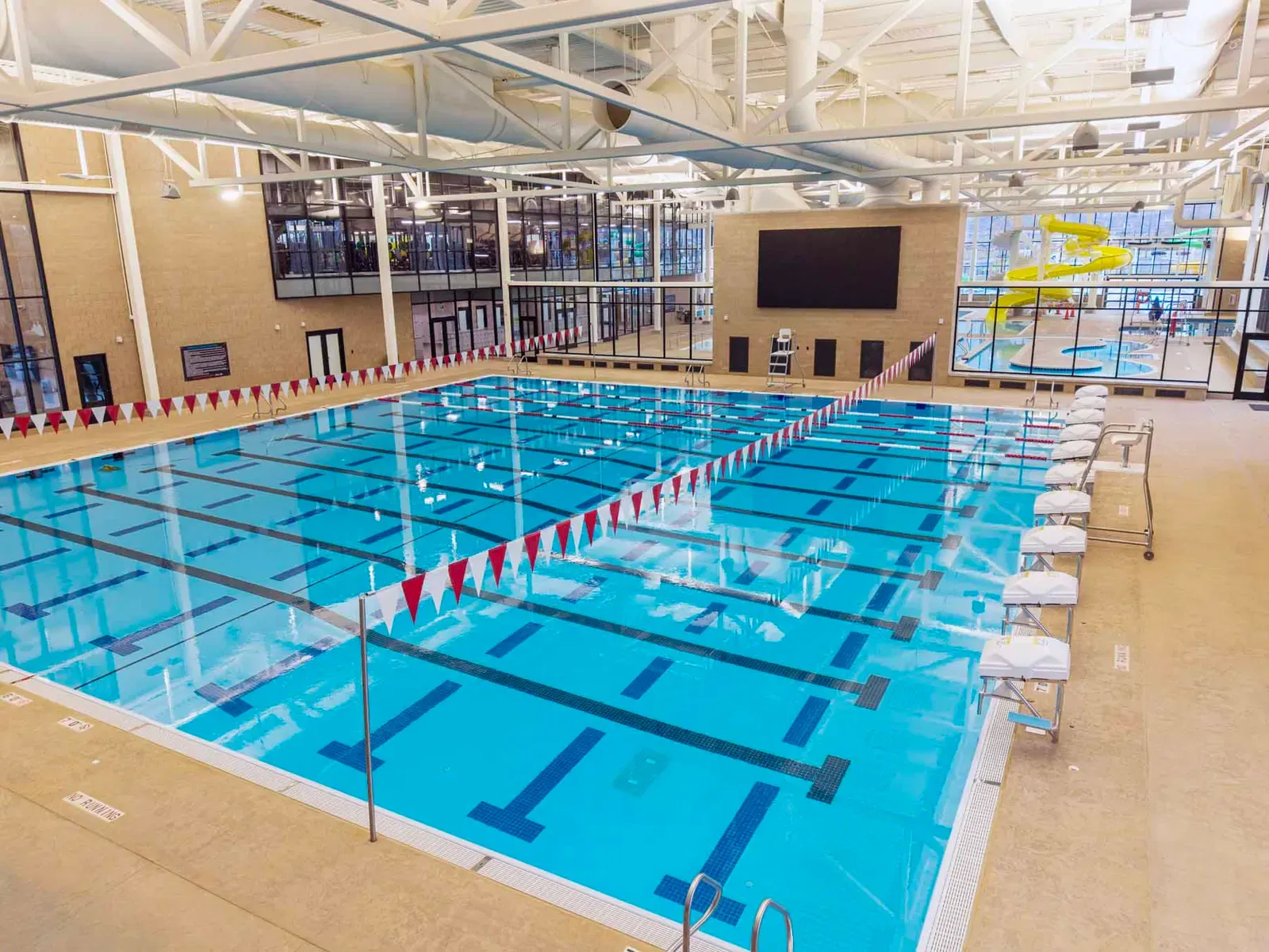 Indoor competition pool with marked lanes and backstroke flags, and a yellow water slide visible in the background.