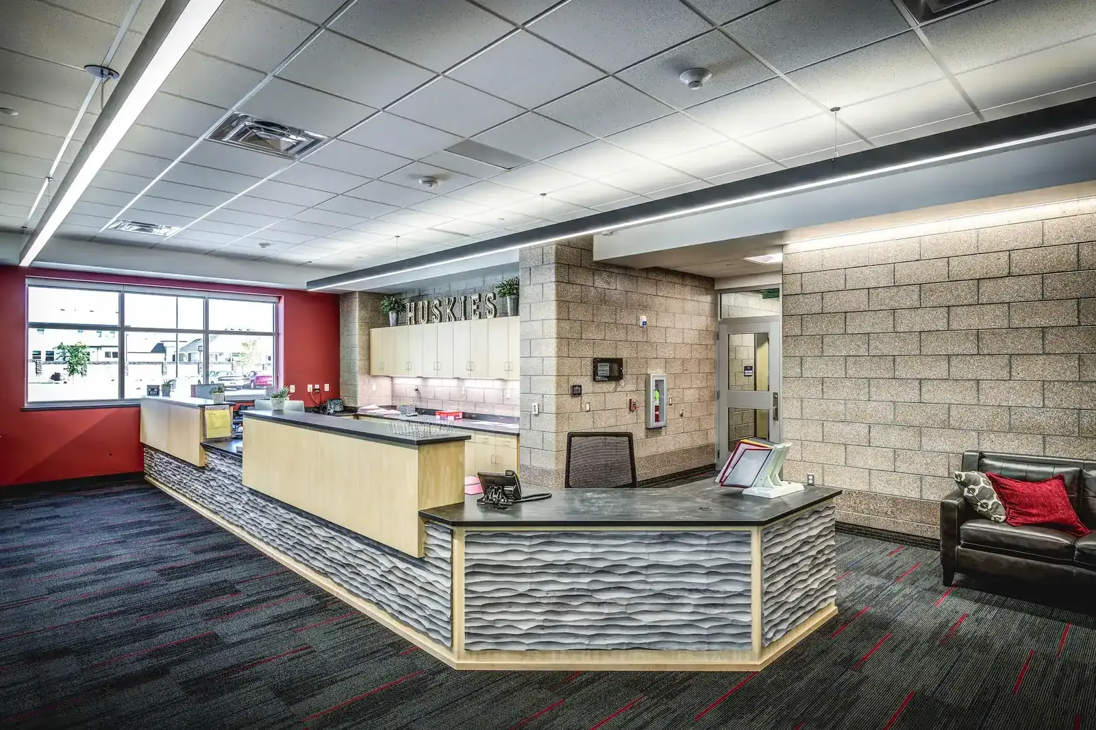 Front office with a curved reception desk, a HUSKIES sign and a red accent wall