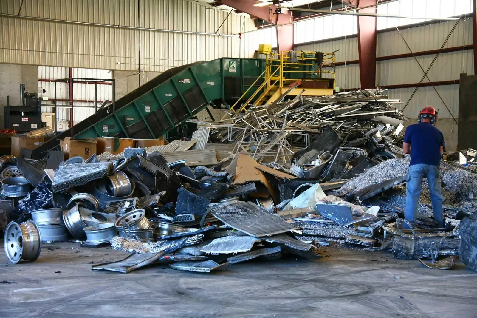 Worker standing beside a pile of scrap metal inside the recycling building.