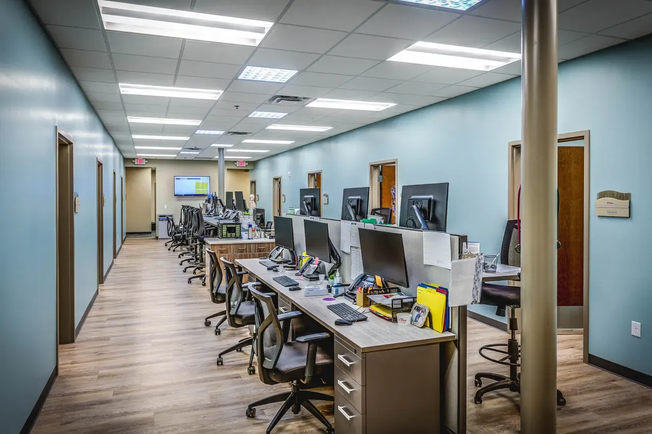 Staff workstations in a long room with teal walls and wood-look flooring.