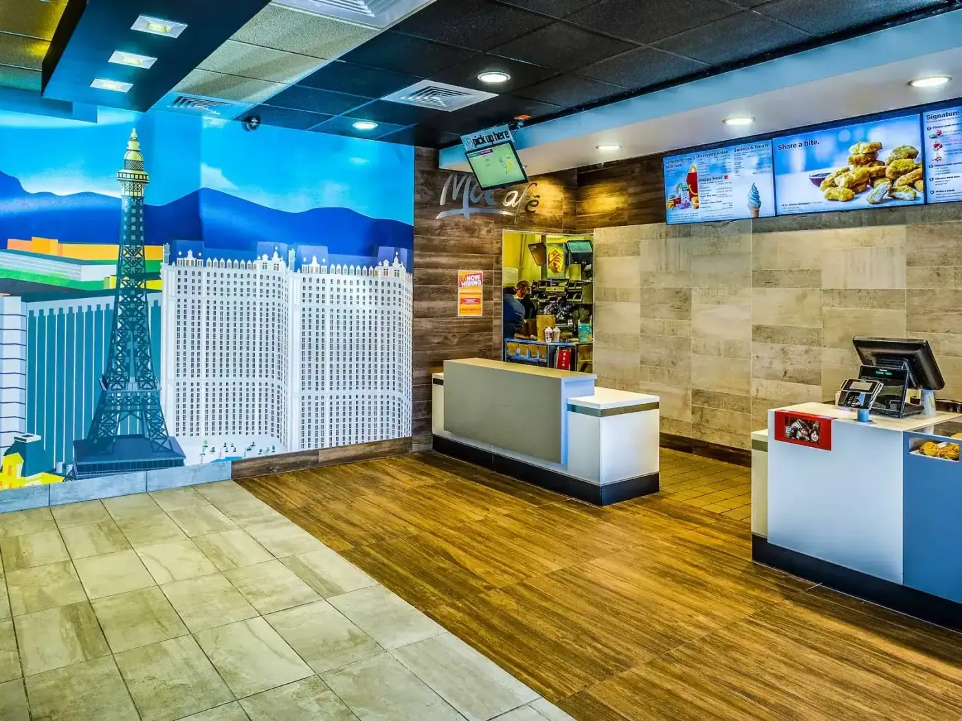 Front counter with a Las Vegas skyline mural, wood-look flooring and digital menu boards.