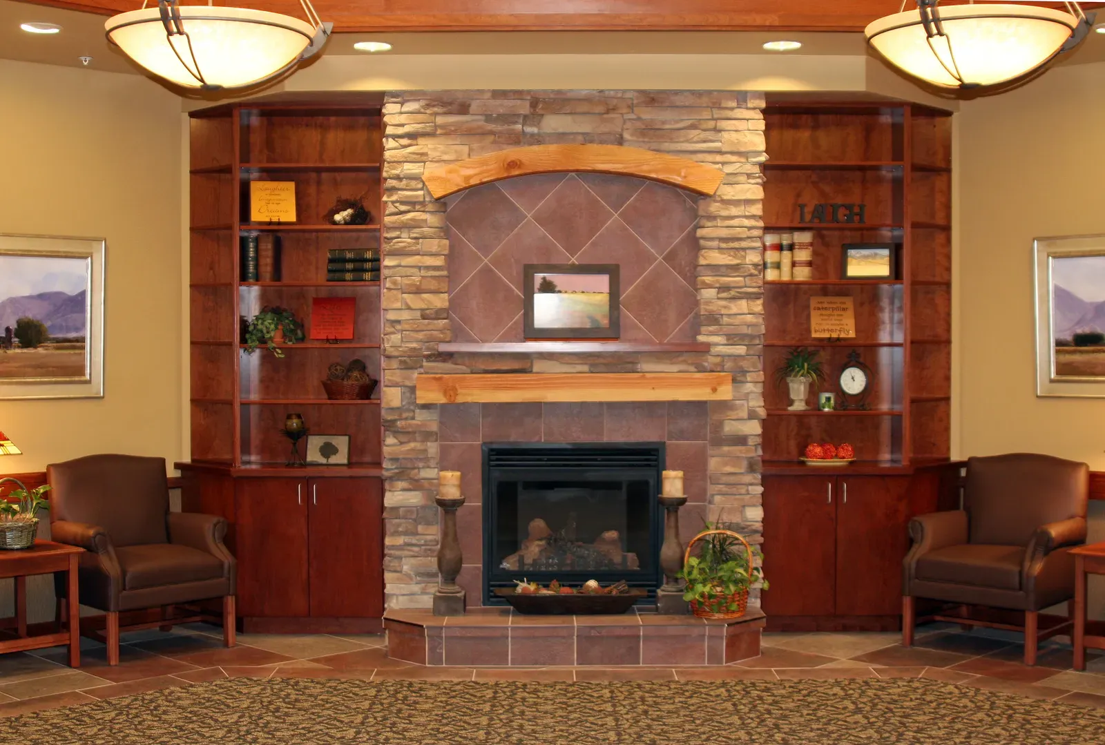 Lobby with a stone fireplace, built-in bookshelves, two leather armchairs and framed landscape paintings.