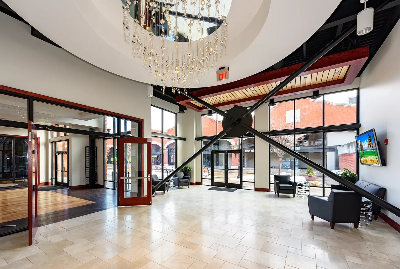Entry lobby with a large round chandelier, black steel cross-bracing and a stone tile floor.