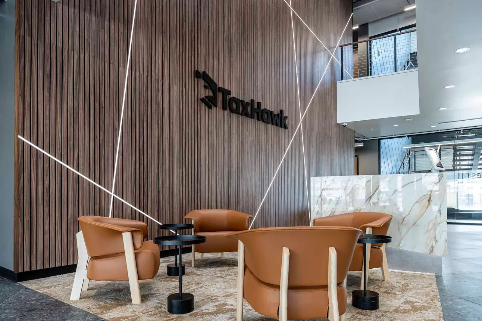 Lobby with a wood-slat wall, a TaxHawk logo, tan leather chairs, and a marble reception desk.