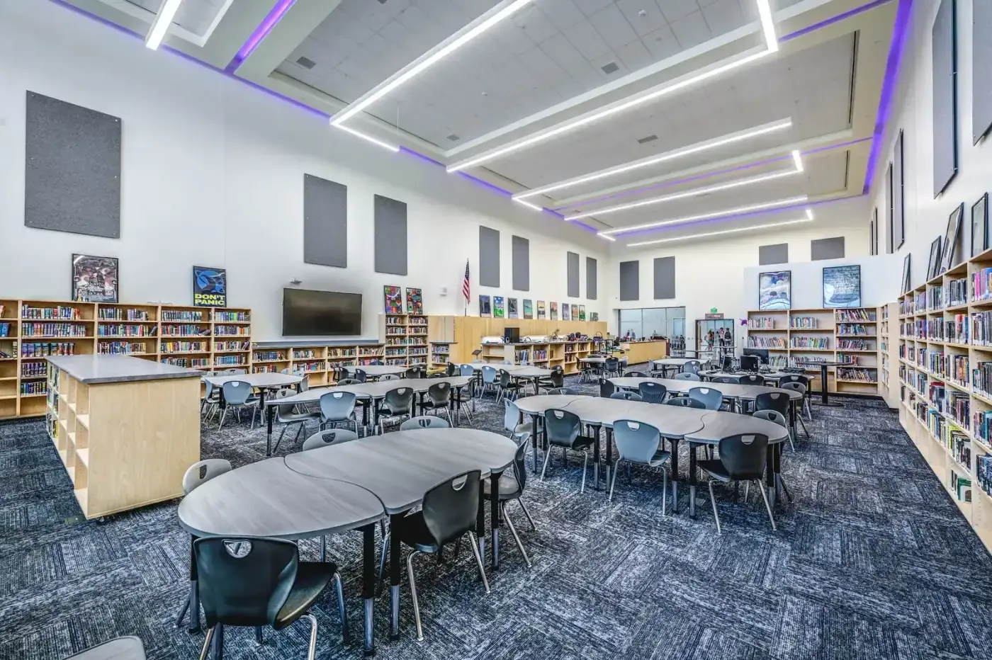 Library with curved tables, bookshelves and ceiling lights outlined in purple.