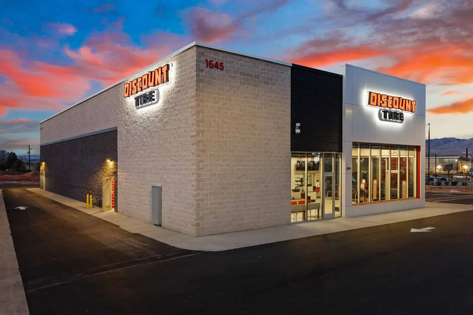 Corner of a Discount Tire store at dusk with glowing signs and a lit storefront
