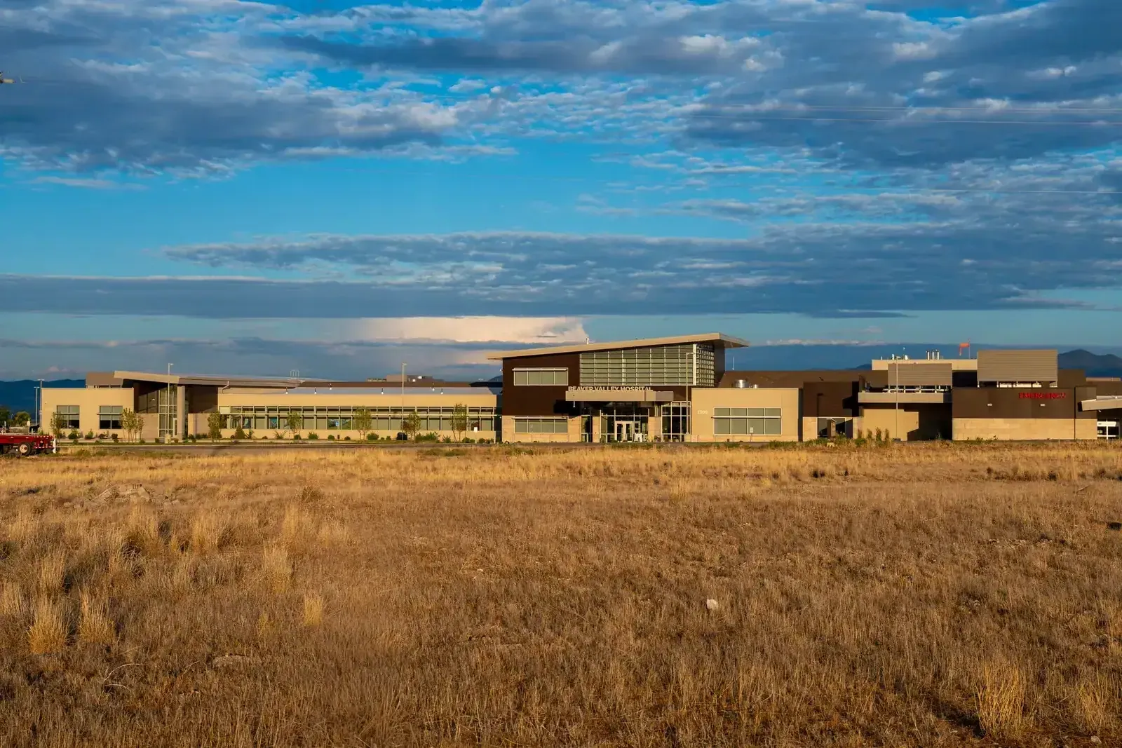 Wide view of the hospital's low wings across a grass field under a blue sky with clouds.