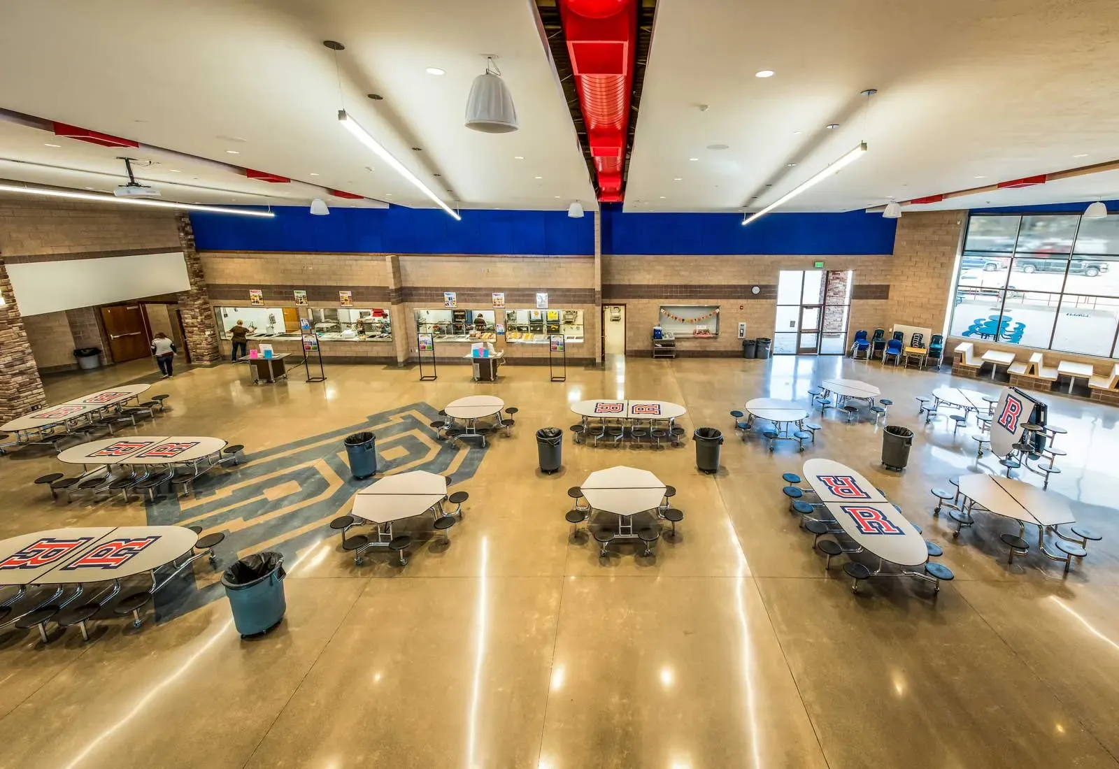 Cafeteria seen from above, with round and rectangular tables, a serving line and large windows