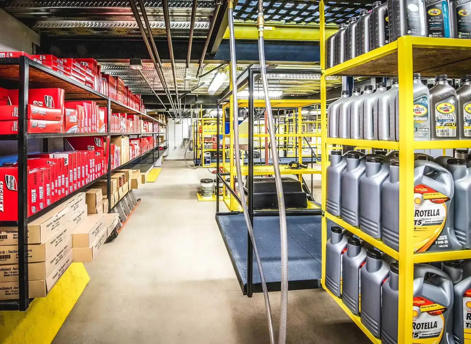 Basement aisle with shelves of motor oil jugs and boxed filters between yellow racking.