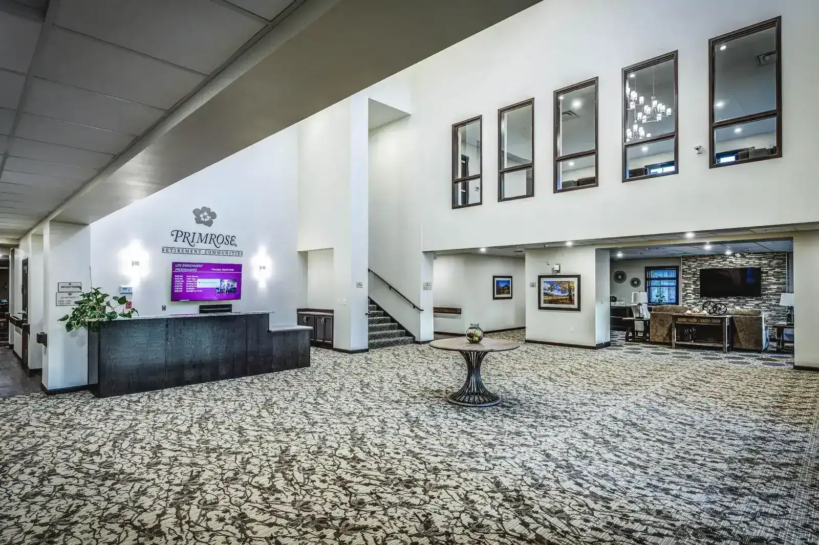 Lobby with a reception desk, a Primrose sign, a staircase and a tall window wall.