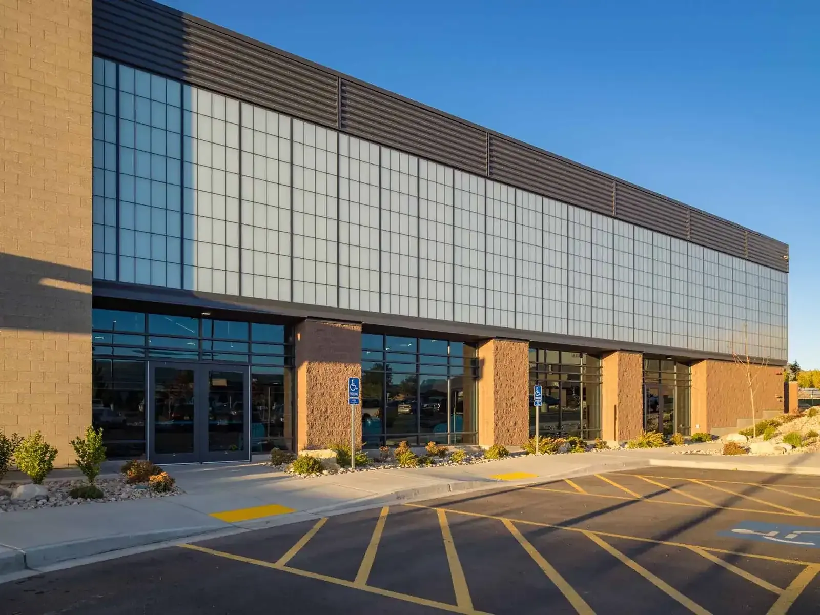 Long translucent glass-panel facade above brick columns and entrance doors, with a parking lot in front.