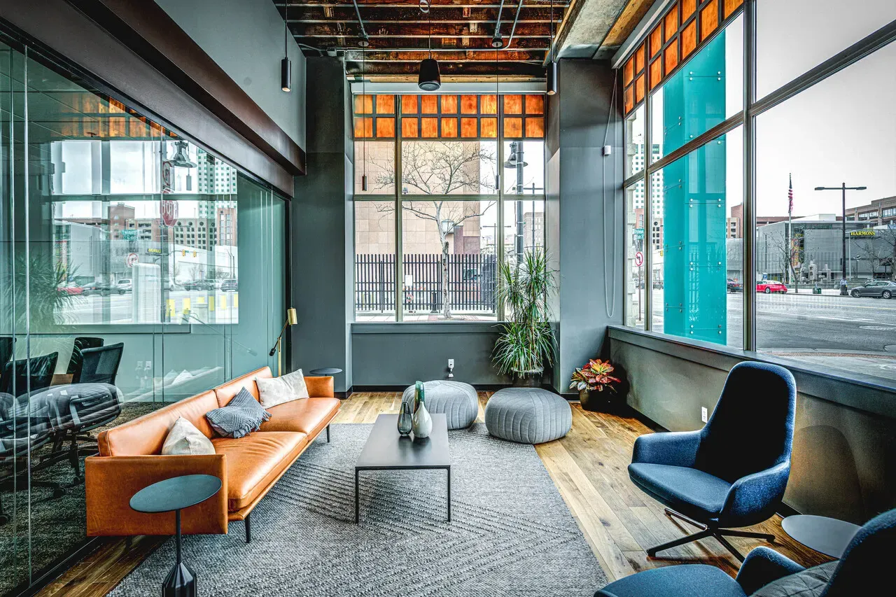 Seating area with an orange leather sofa and blue armchairs beside large street-facing windows.