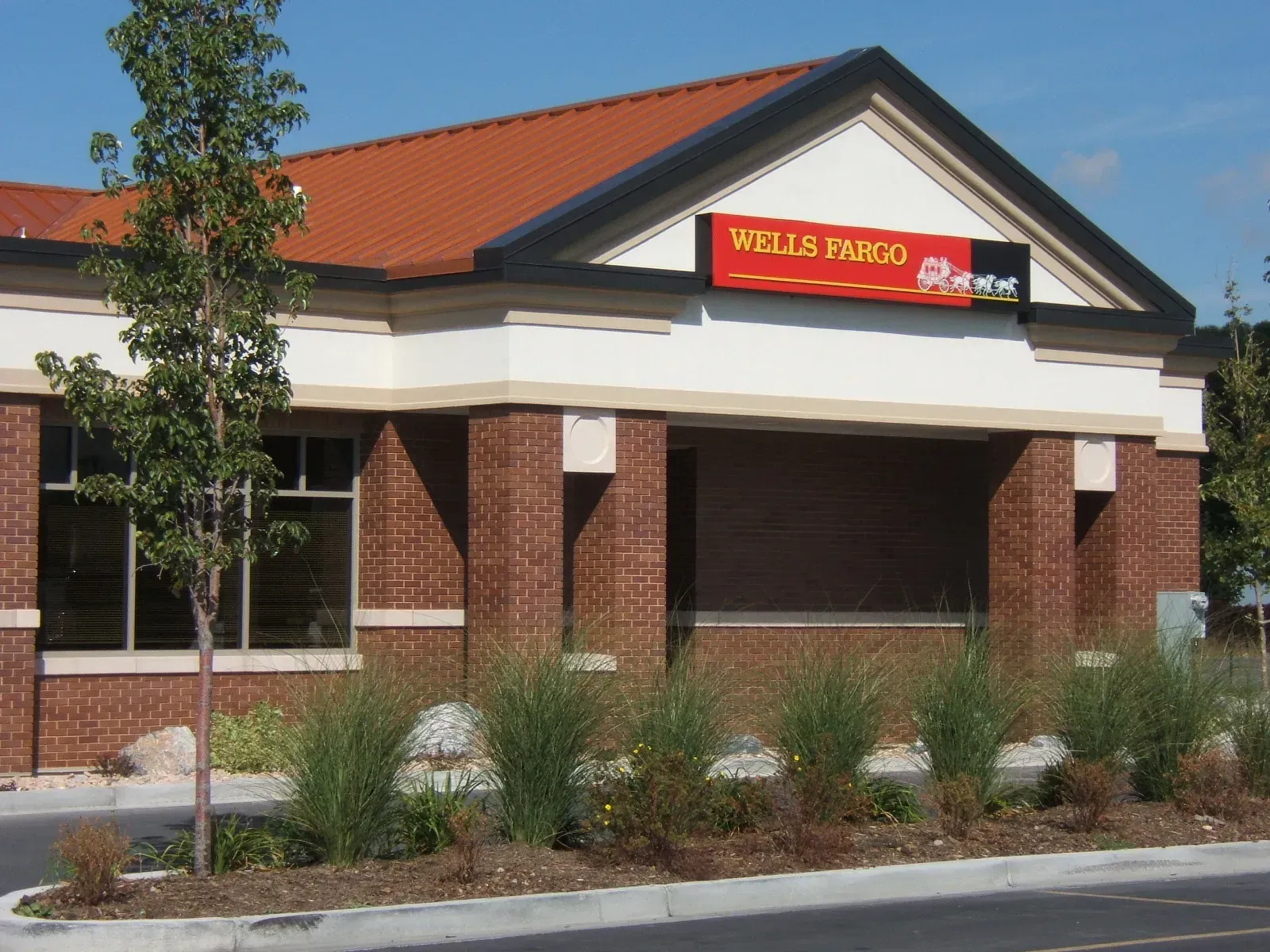Close view of the branch entry with a red Wells Fargo sign, brick columns and ornamental grasses in front.