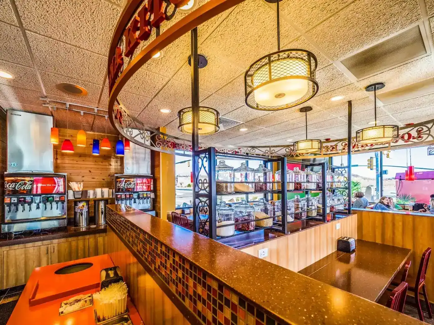 Dining room counter with soda dispensers, a curved decorative rail and shelves of condiment jars.