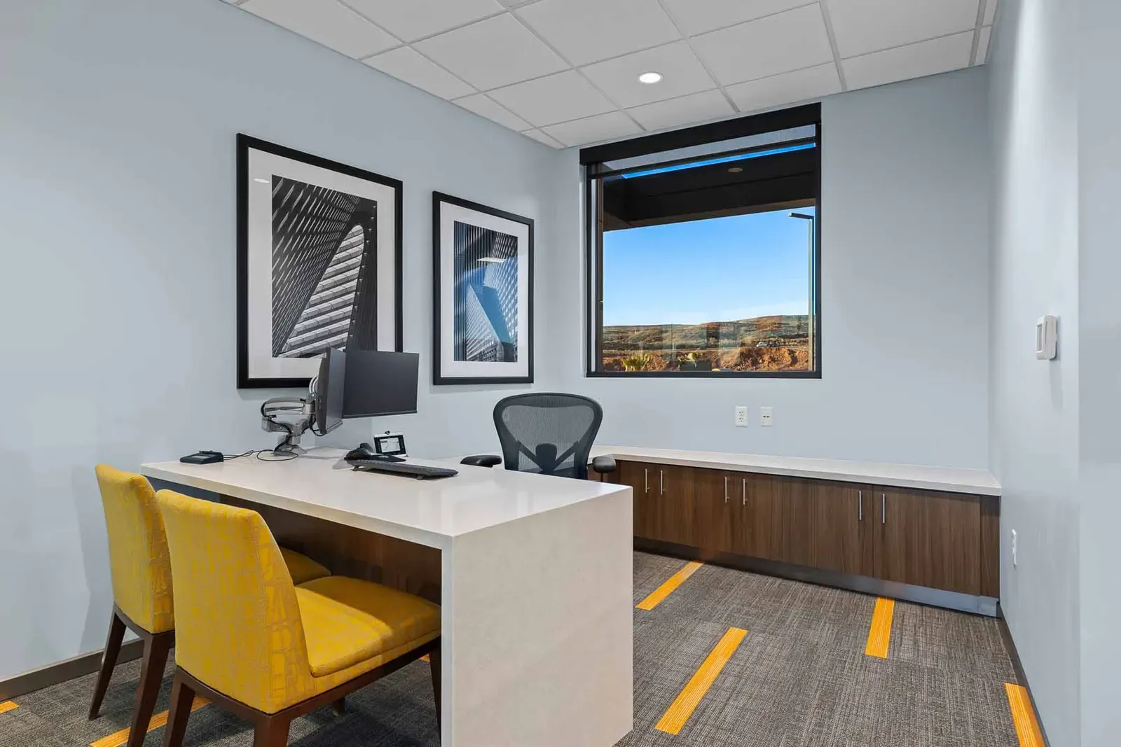 Private office with a white desk, yellow chairs, and framed black and white photos.