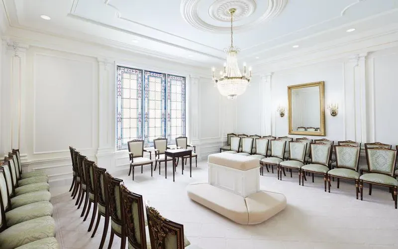 Sealing room with a central cushioned altar, rows of green upholstered chairs, a gold-framed mirror and a stained-glass window
