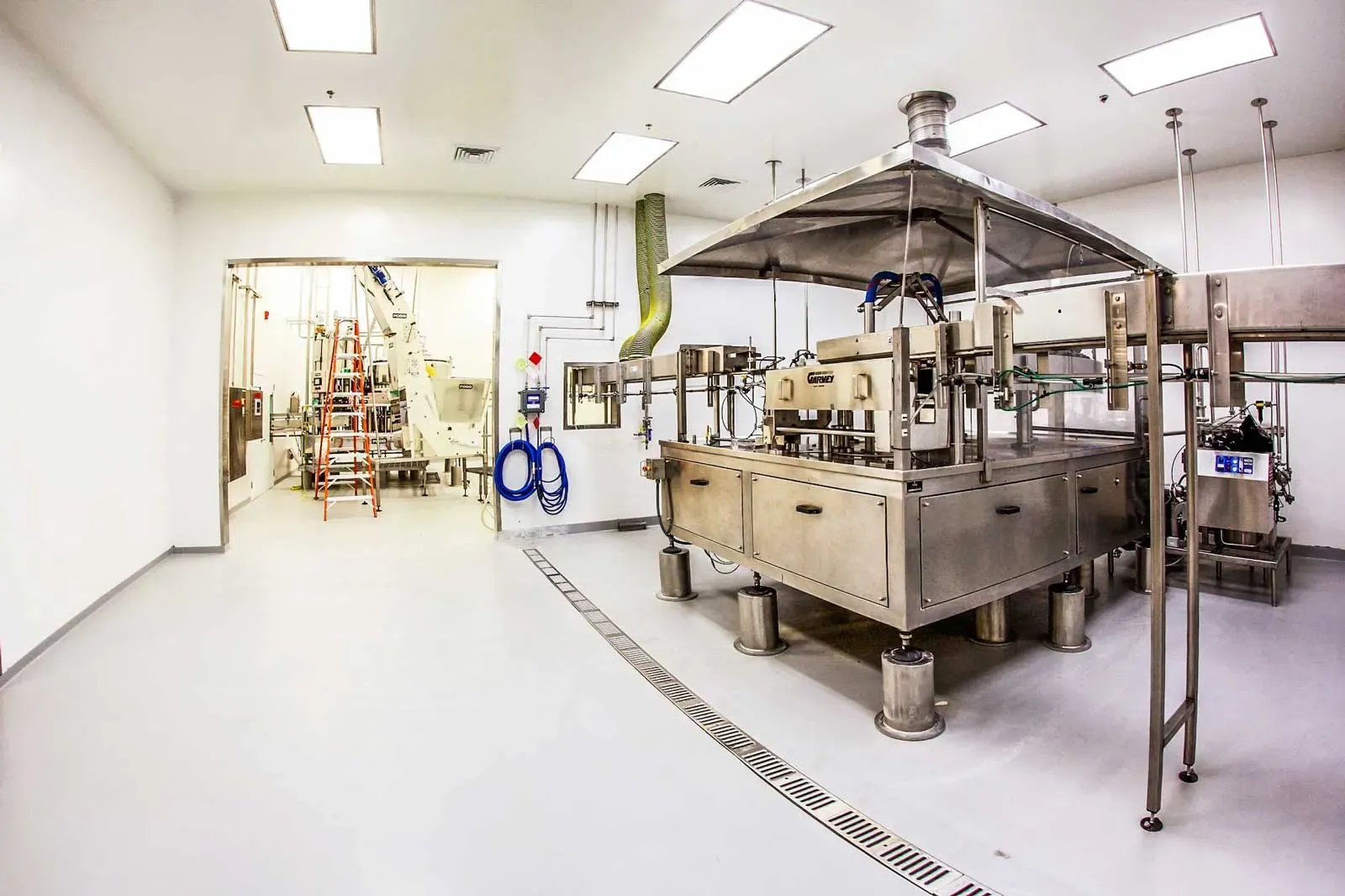 Processing room with stainless steel equipment and a floor drain, with a larger production area beyond.