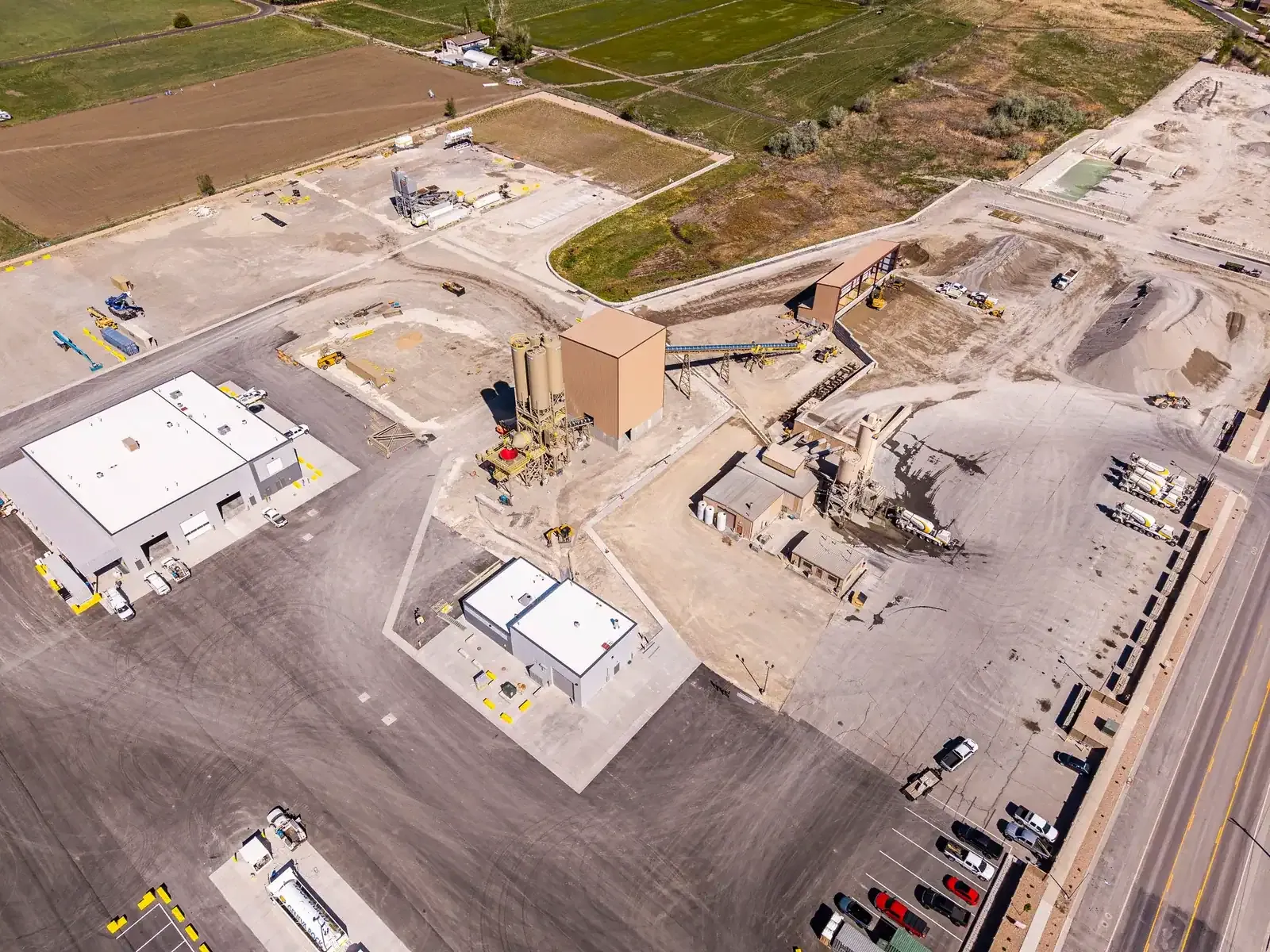 Aerial view of the site with white-roofed buildings, silos, aggregate piles and a paved yard.