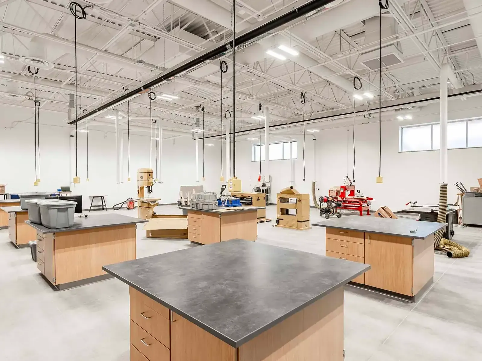 Shop classroom with wood workbenches and woodworking machines under a high steel-truss ceiling