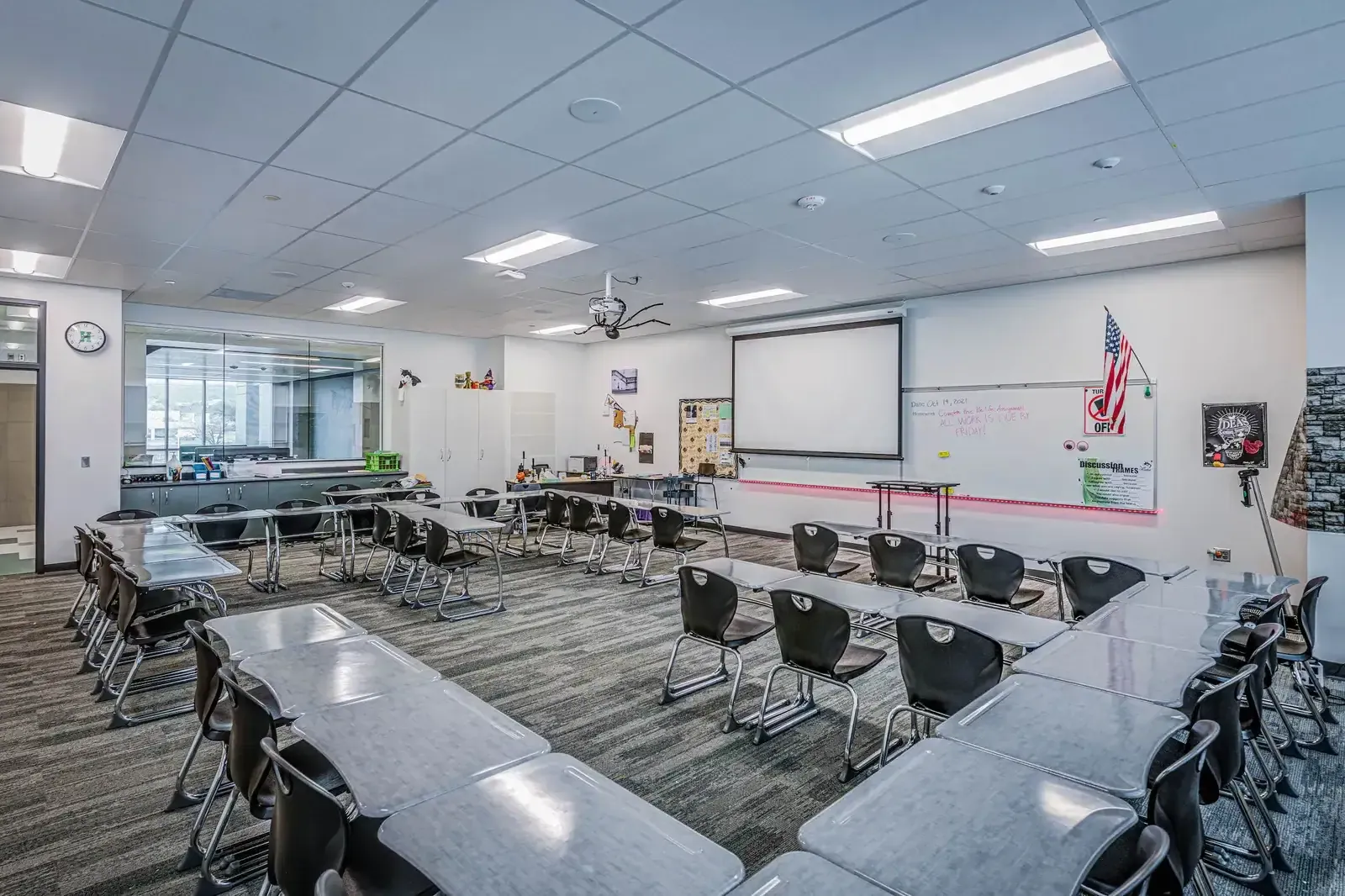 Classroom with grouped tables, black chairs, a projection screen and a whiteboard