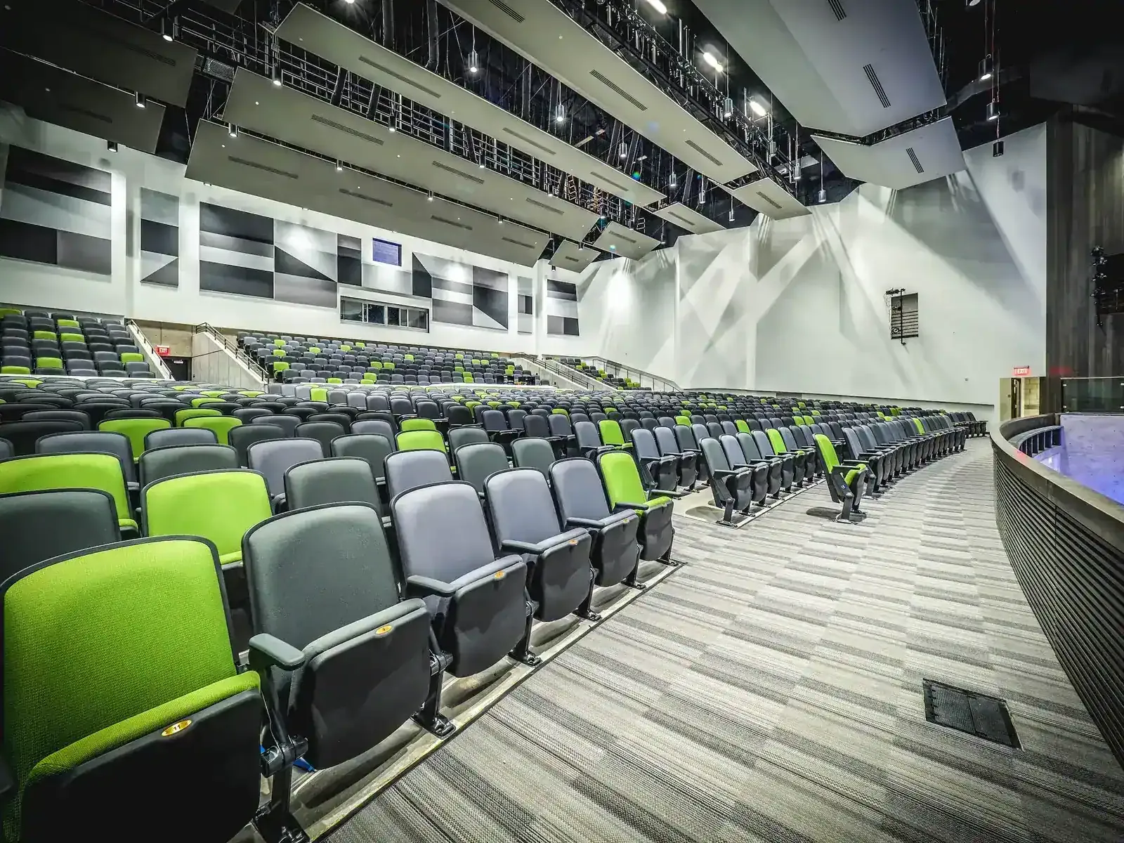 Auditorium seating in green and gray with a curved balcony front and acoustic wall panels