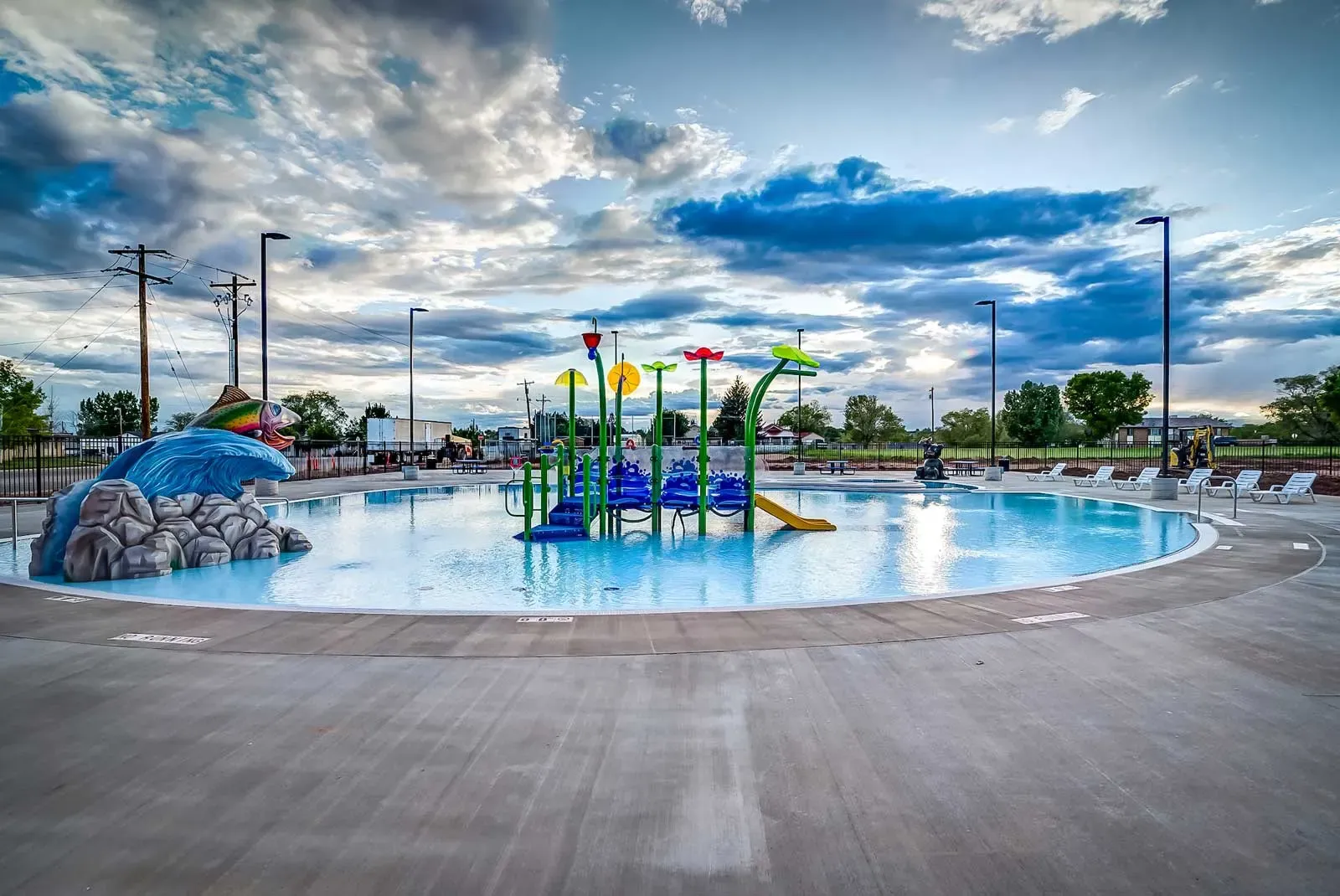 Outdoor splash pad with colorful water features and a rock-style slide under a cloudy sky