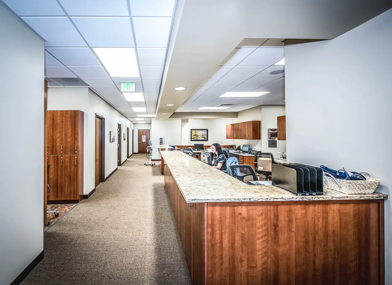Long granite-topped reception counter with wood panels and a hallway of offices beyond.