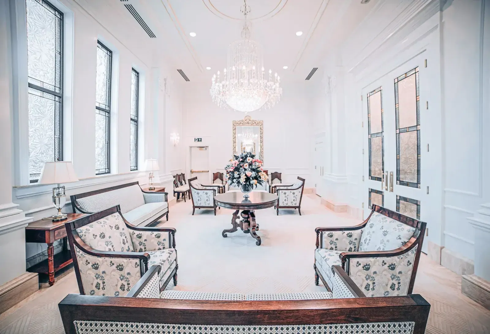 Sitting room with a crystal chandelier, floral-upholstered chairs and a round table holding a flower arrangement.
