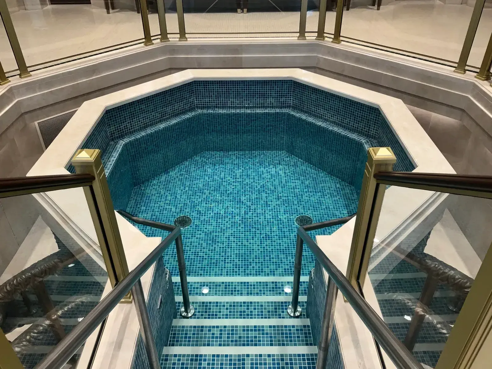 Baptismal font lined with blue mosaic tile, with steps, handrails and glass and brass railings around it.