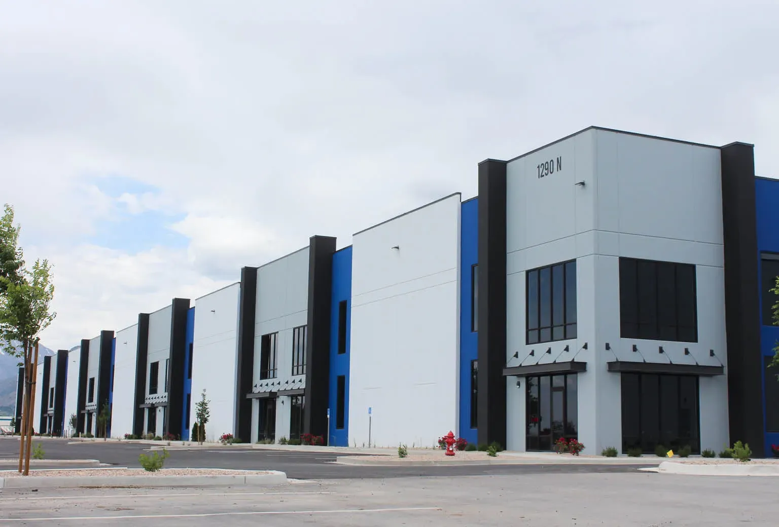 Row of industrial buildings with gray, blue, and black panels, marked 1280 N, along a parking lot.