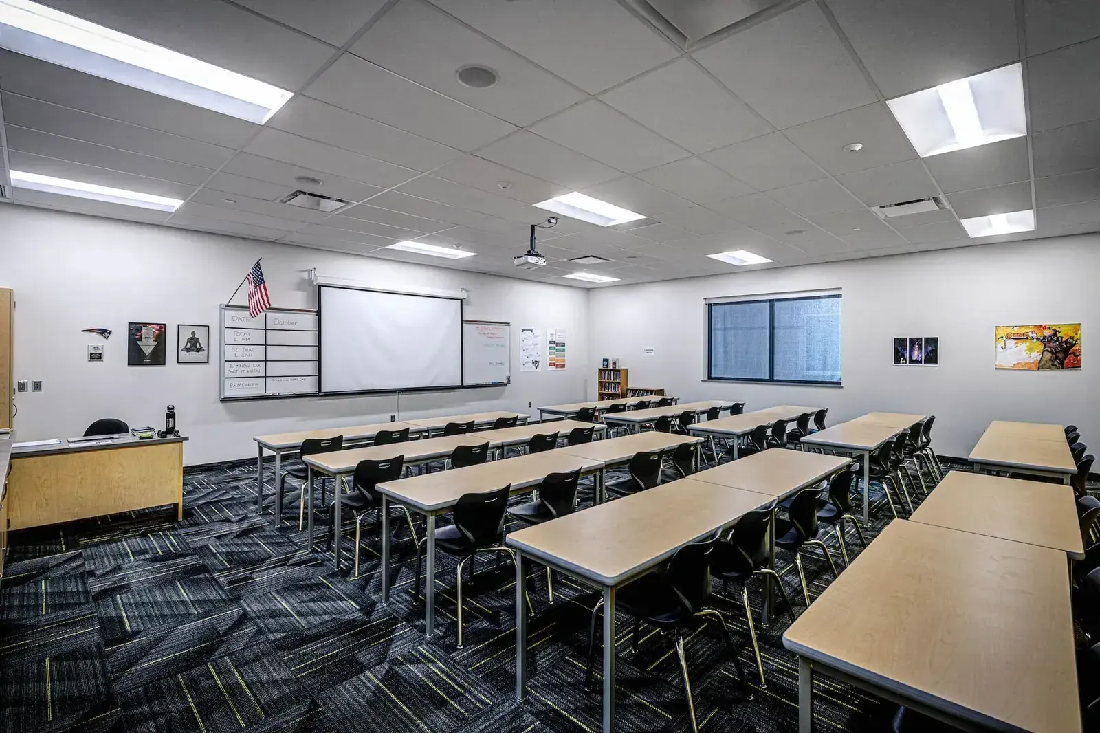 Classroom with long tables, black chairs, a whiteboard, and patterned carpet.