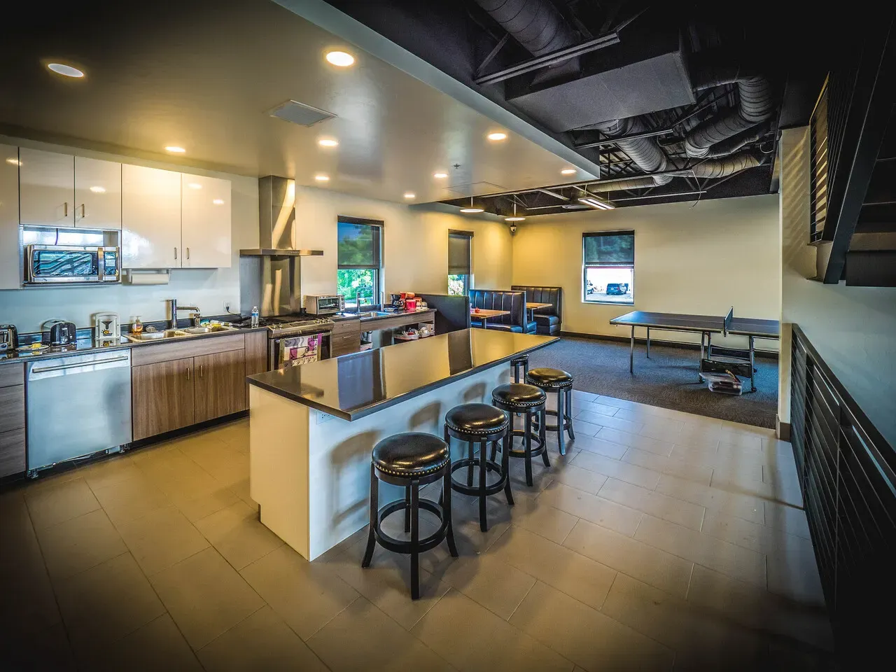 Kitchen with an island and stools, and a ping-pong table in the background