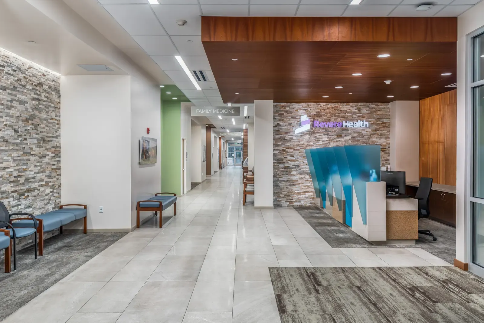 Reception lobby with a stacked-stone wall, a wood ceiling soffit and the Revere Health sign above the front desk