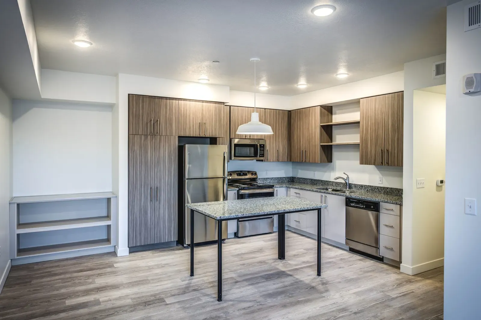 Apartment kitchen with wood-tone cabinets, stainless steel appliances and a granite-topped table.