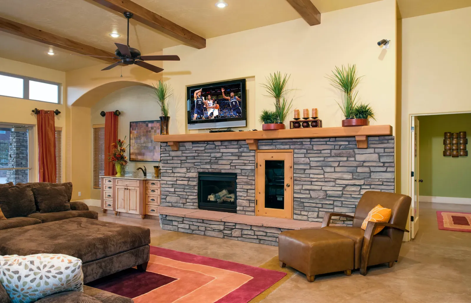 Clubhouse great room with a stone fireplace, a wood mantel, exposed ceiling beams and leather and fabric seating.