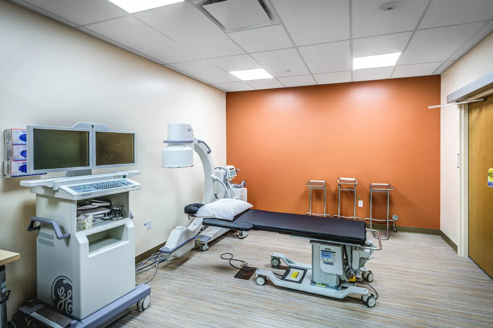 Procedure room with an adjustable table, C-arm imaging equipment and an orange accent wall