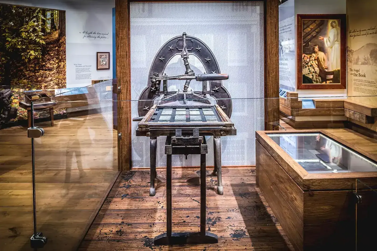 Exhibit with a historic hand printing press behind glass, next to a wood-framed display case