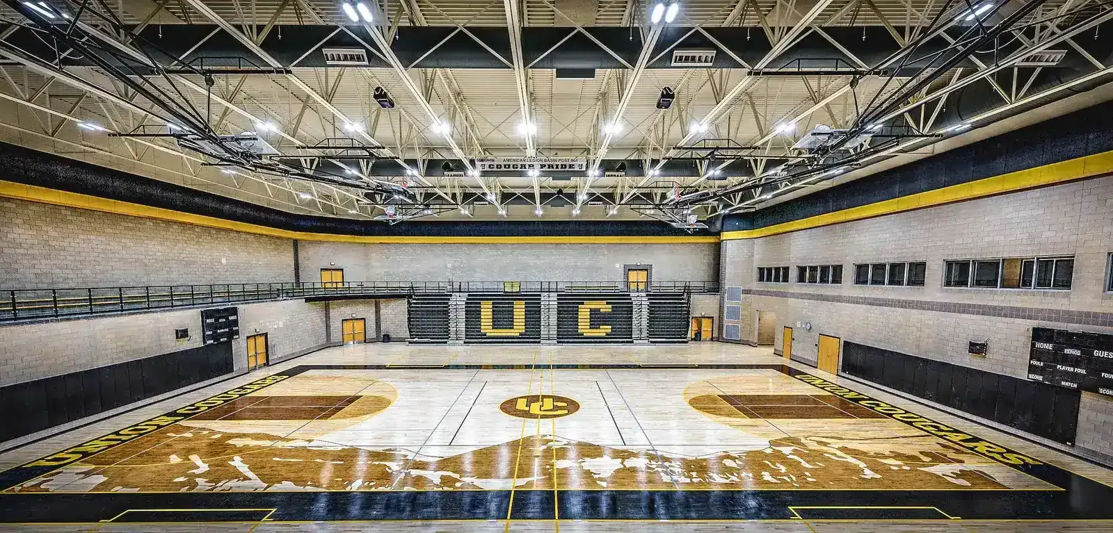 Gymnasium with a wood floor, black and gold walls and an upper walkway.