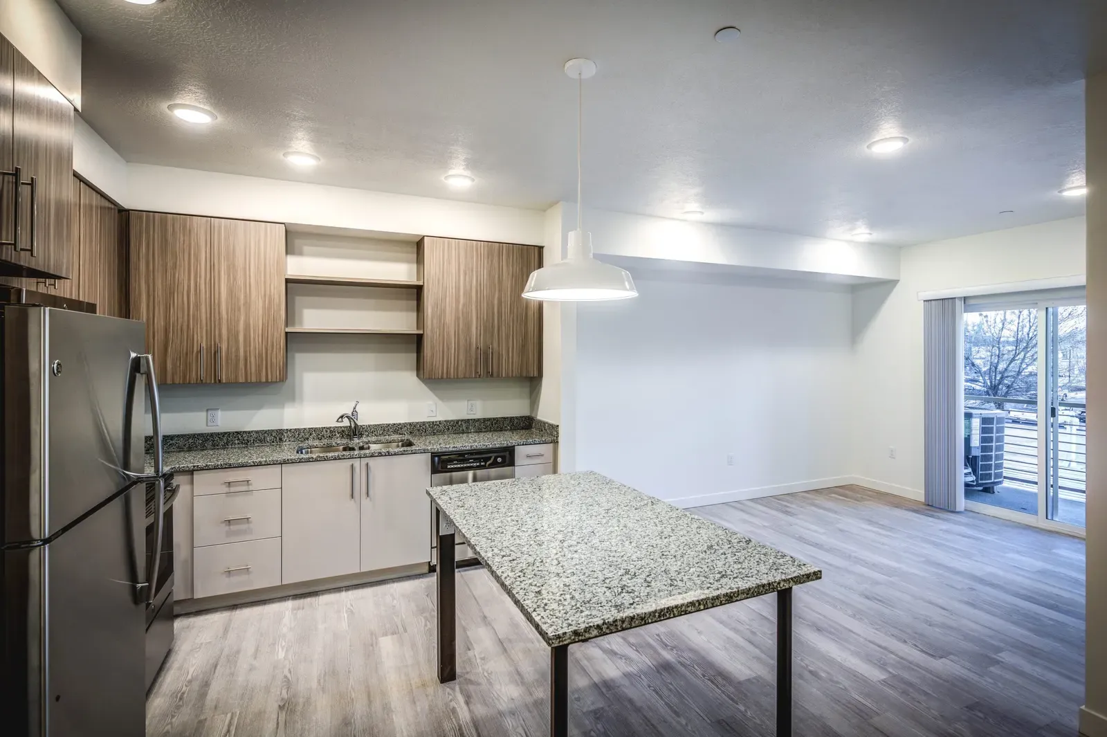 Open apartment kitchen and living area with a granite-topped table and a sliding door to a balcony.