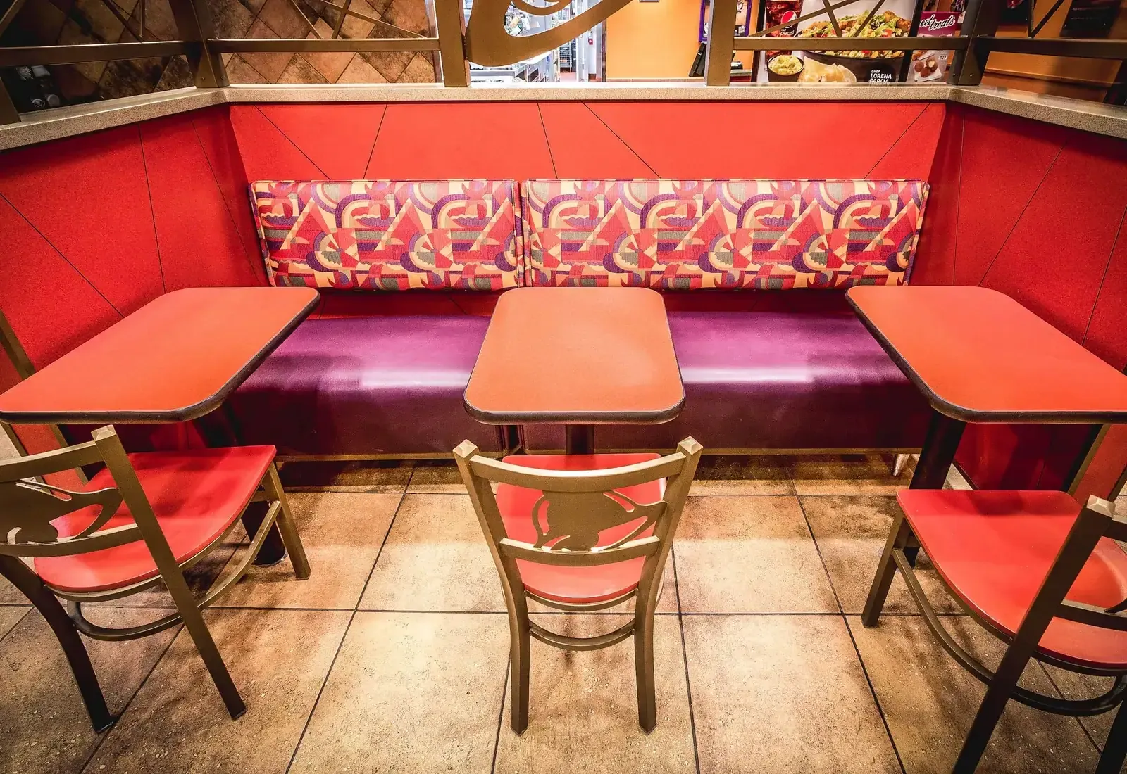 Booth seating with patterned upholstery, red tabletops and metal chairs