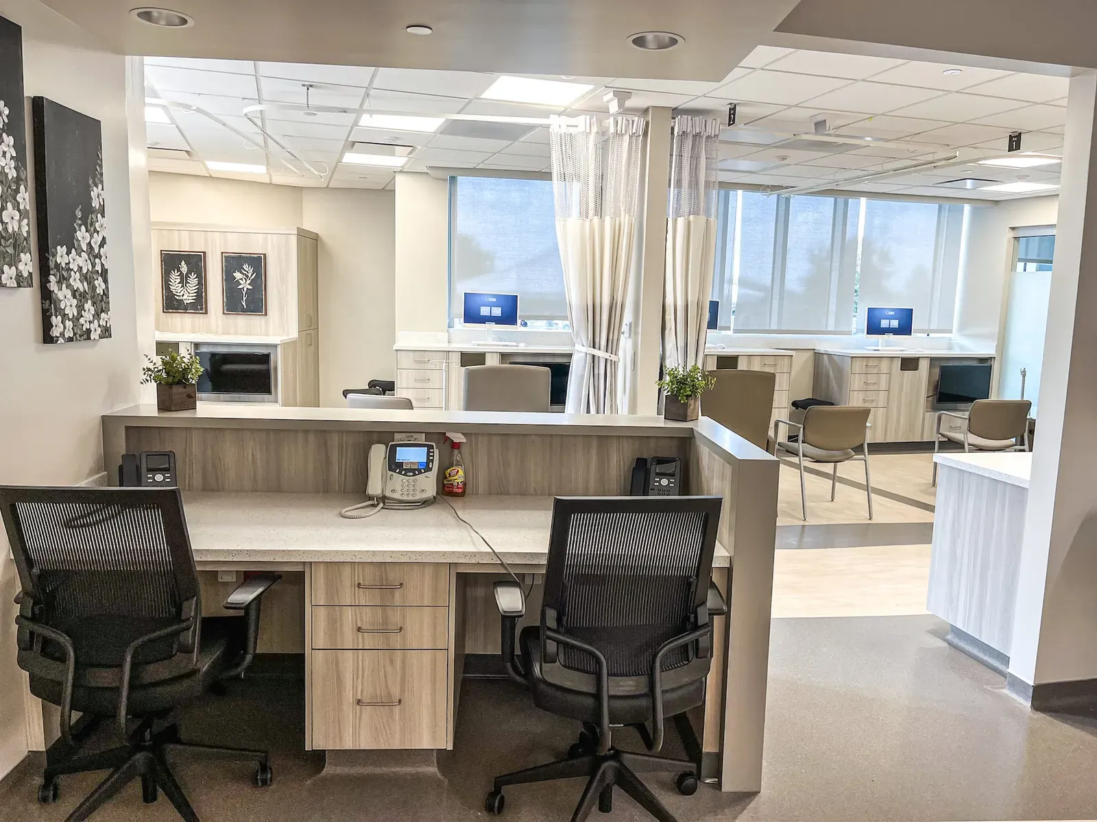 Nurse station with two desk chairs and curtained patient bays beyond