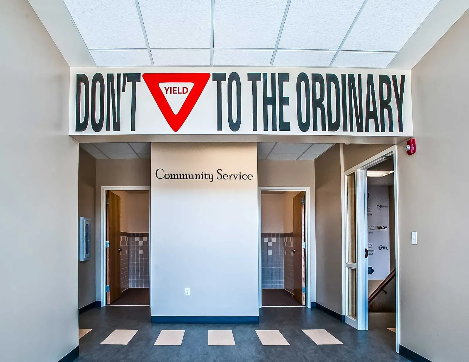 Office entry hall with a large wall sign reading "Don't Yield to the Ordinary" above two doorways